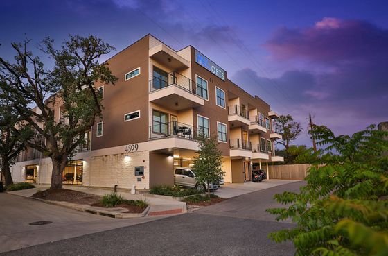 Elegant multi-story apartment building with modern balconies set against a stunning evening sky, surrounded by lush greenery.