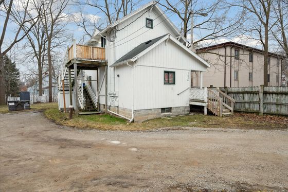 Charming white house with rustic wooden stairway and spacious backyard, offering serene surroundings and inviting outdoor space.