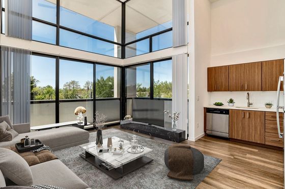 Bright and modern apartment living room with large floor-to-ceiling windows offering a scenic view, stylish furnishings, and a sleek, open-concept kitchen.