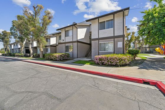 Charming apartment building with lush landscaping and vibrant flowers, nestled in a serene residential area with a clear blue sky.