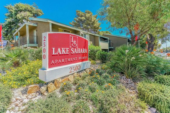 Vibrant exterior view of Lake Sahara Apartment Homes, featuring lush landscaping, a bold red sign, and a welcoming entrance.