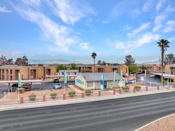 Charming apartment complex featuring architectural elegance, ample parking, and beautiful landscaping under a vibrant blue sky.
