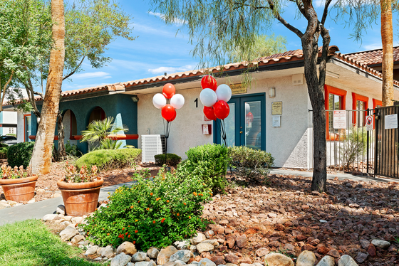 Inviting leasing office entrance adorned with vibrant red and white balloons, surrounded by lush greenery and vibrant landscaping.
