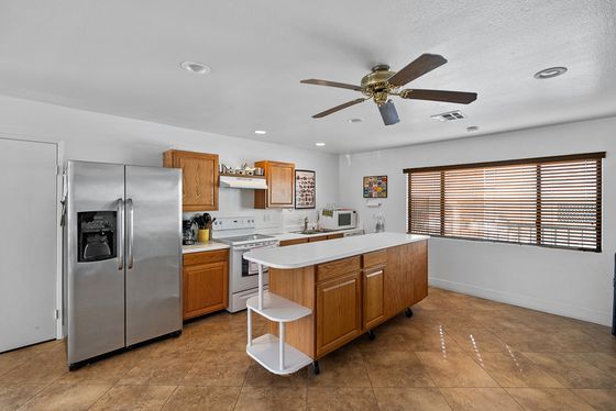 A spacious, open-concept kitchen with a large breakfast bar island, stainless steel refrigerator, and wood-style flooring.