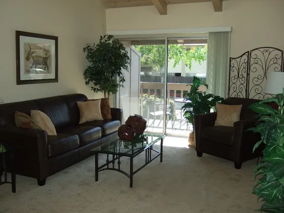carpeted living room with leather sofas and a metal and glass coffee table at plumas garden apartments