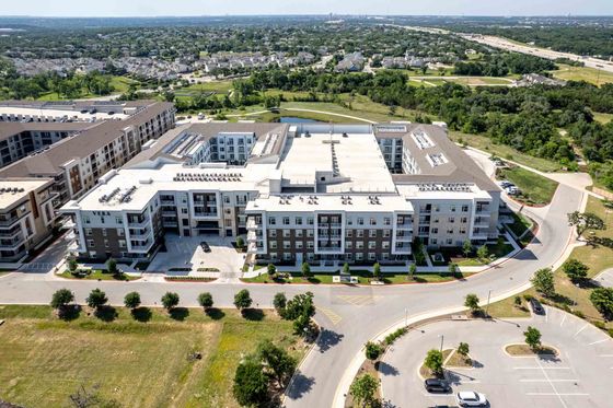 Aerial view of a modern apartment complex surrounded by lush greenery, showcasing a well-planned urban neighborhood with easy access to main roads.