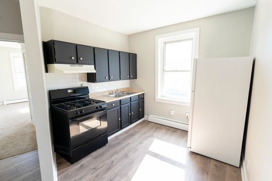 beautiful kitchen with large window, wood floor, fridge and stove, and black cabinets