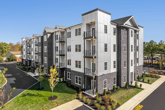 Modern apartment complex with sleek architecture, large windows, and private balconies surrounded by lush landscaping.