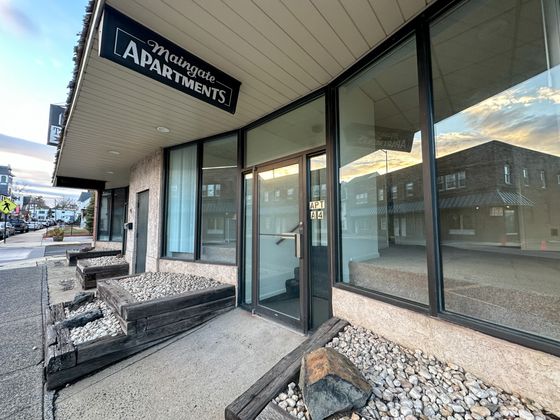 Inviting entrance of Maingate Apartments with large glass windows and rustic stone landscaping, showcasing urban living charm.