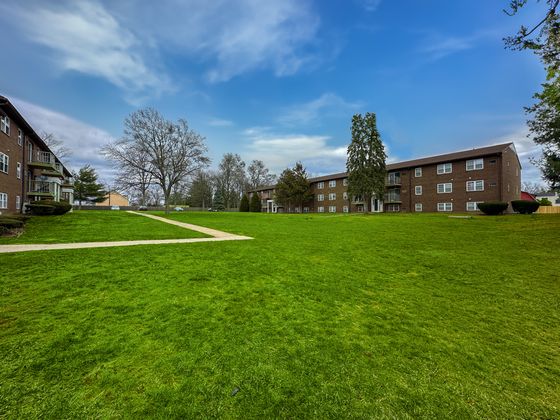 Spacious apartment buildings surrounded by lush green lawns and serene pathways under a clear blue sky.