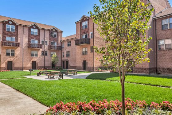 Inviting apartment complex courtyard with lush greenery, vibrant flower beds, and picnic benches, offering a serene outdoor space for residents.