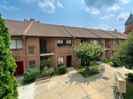 Charming townhouse featuring classic brick exterior, lush green landscape, and serene outdoor seating area.