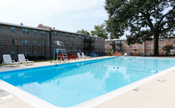 Inviting apartment complex with a sparkling outdoor pool, surrounded by sun loungers and lush greenery, perfect for relaxation.