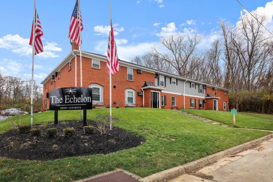 Inviting exterior view of The Echelon Luxury Apartments, featuring a classic brick facade and lush green landscaping, under a bright blue sky.