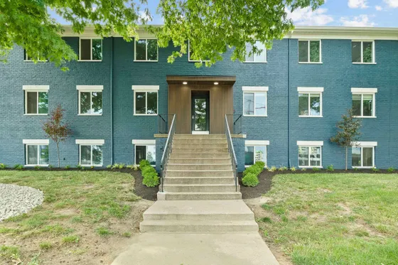 Charming apartment building with a stylish blue brick facade, featuring a welcoming entrance and manicured landscaping.
