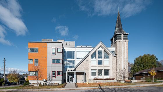 Charming modern building with a mix of wood and stone facade, featuring a distinctive tower against a clear blue sky.