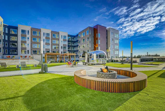 Modern apartment complex with vibrant outdoor space featuring a cozy fire pit, colorful seating, and stylish landscaping under a clear blue sky.