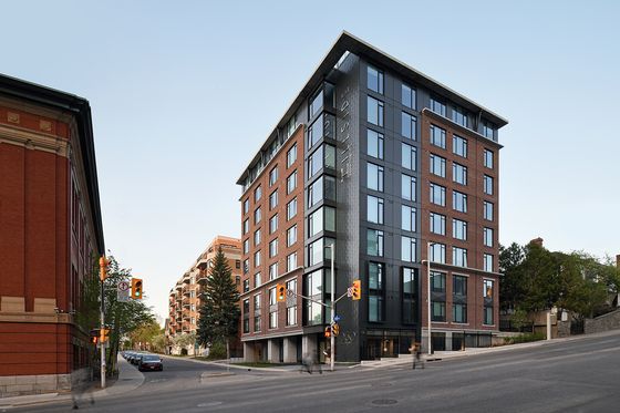 Modern urban apartment building with sleek design, large windows, and stylish exterior, located at a bustling street corner.