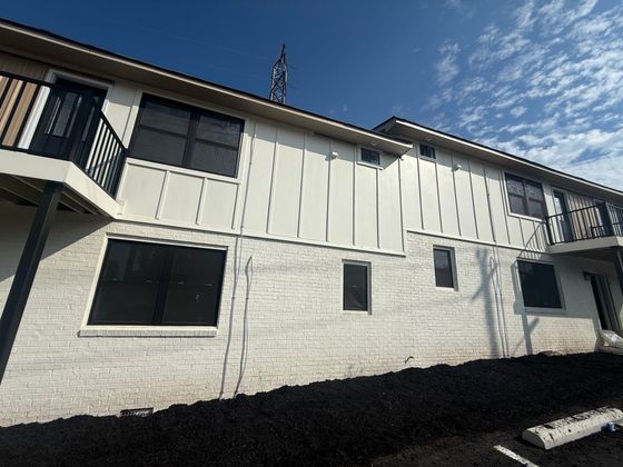 Charming apartment exterior showcasing a modern two-story design with large windows and sleek black railings under a clear blue sky.