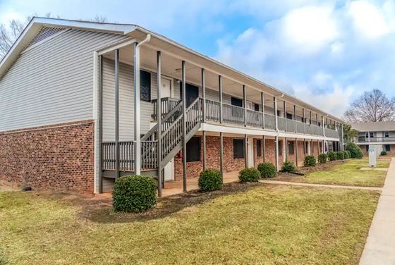 Charming two-story brick apartment with modern balconies and lush green surroundings.