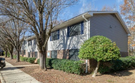 Charming apartment building with classic brick facade and lush landscaping, surrounded by mature trees and set in a serene neighborhood.