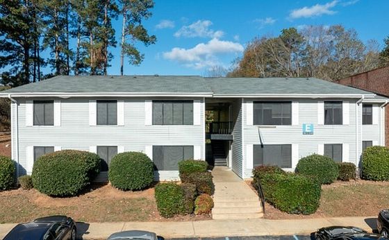 Charming two-story apartment building surrounded by lush greenery, offering ample parking and a peaceful neighborhood vibe.