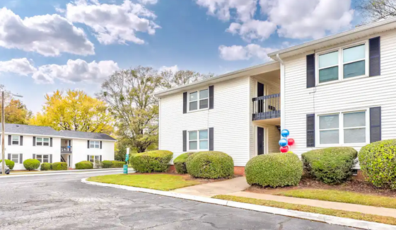Charming apartment complex with vibrant landscaping, featuring white two-story buildings and a bright sky backdrop.