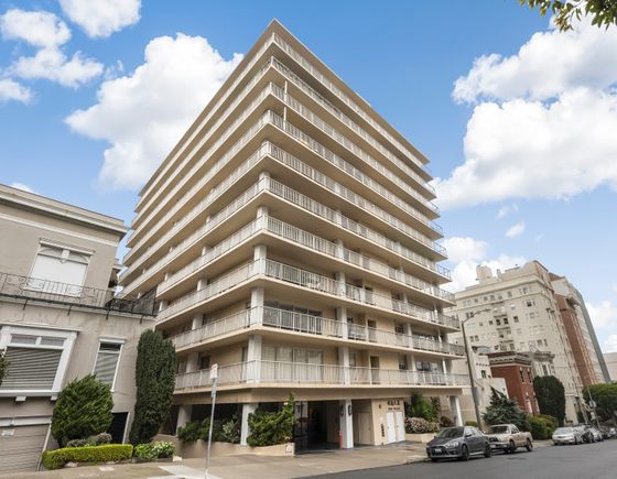 Elegant high-rise apartment building with modern balconies, set against a vibrant blue sky, offering urban living at its finest.