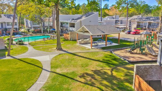 Vibrant apartment community with a refreshing pool, modern picnic area, and family-friendly playground surrounded by lush greenery.