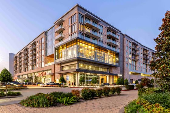 Modern multi-story apartment building with illuminated glass facade and vibrant street life in an urban setting.