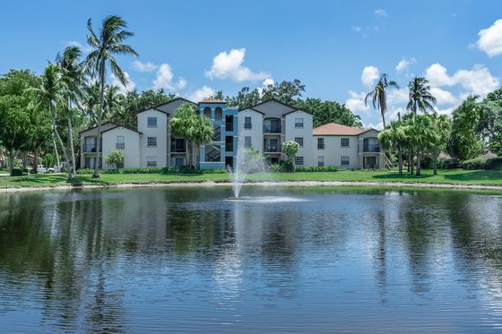 Picturesque lakeside apartment complex with lush greenery and a central water fountain.