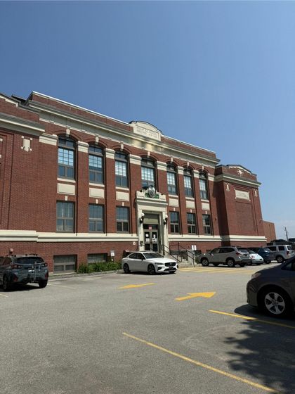 Charming historic brick building with elegant architectural details, ample parking, and a clear blue sky backdrop.