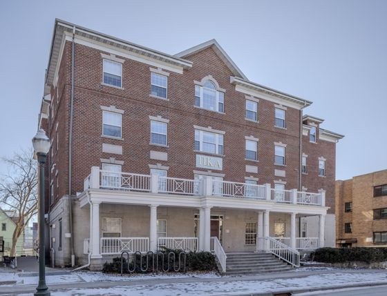 Charming red-brick residential building with classic white trim, large windows, and a welcoming front porch, ideal for urban living.
