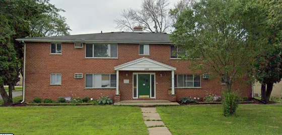Charming red brick apartment complex with lush green lawn and mature trees, offering a serene and inviting living environment.