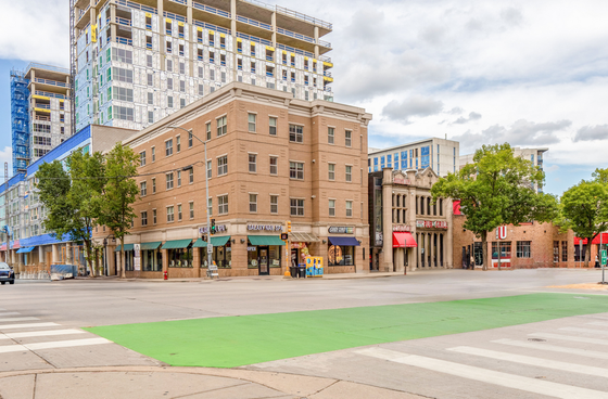 Charming urban street view featuring a classic brick building with vibrant storefronts, set against a modern construction backdrop, ideal for urban living.