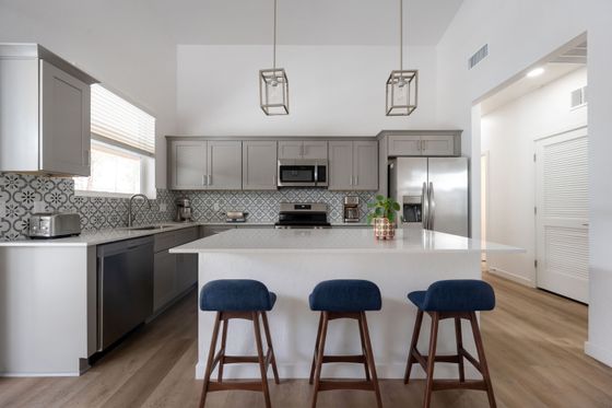 Modern kitchen with elegant gray cabinets, stylish geometric backsplash, and a sleek island with plush bar stools.
