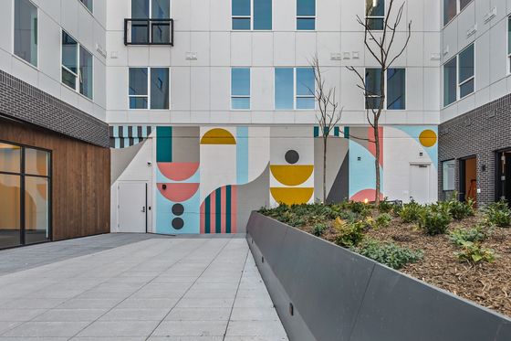 Modern apartment courtyard featuring vibrant geometric wall art, elegant landscaping, and sleek building design.