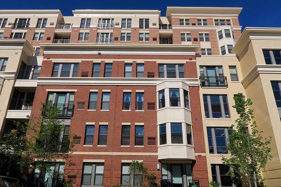 Elegant modern apartment exterior featuring brick and cream facade with large windows and inviting balconies, against a vibrant blue sky.