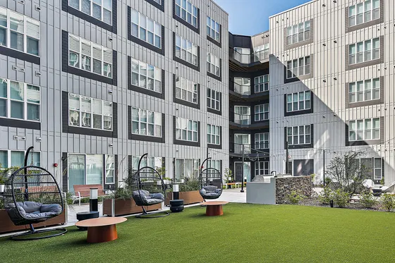 Modern apartment complex courtyard featuring stylish hanging chairs and vibrant green lawn for a relaxing outdoor experience.