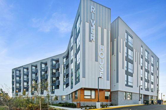 Modern apartment building 'River House' showcasing sleek architecture, large windows, and inviting outdoor landscaping under a clear blue sky.