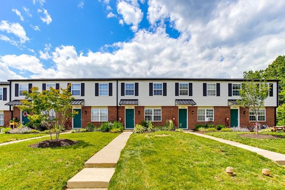 Charming townhouses with classic brick and siding facade, surrounded by lush greenery and bright blue skies.