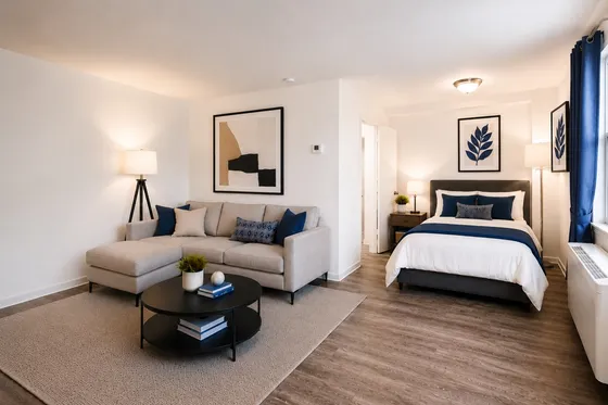 Modern studio apartment featuring a cozy living area with a stylish gray sofa and a chic bedroom with a comfortable bed, complemented by elegant decor and warm lighting.