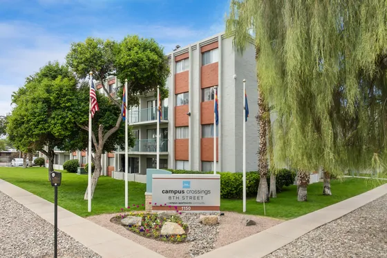 Charming apartment complex with modern design, surrounded by lush greenery and a welcoming entrance at Campus Crossings on 8th Street.