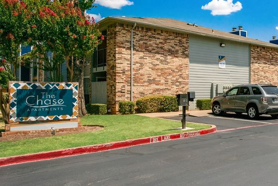 Charming apartment complex with attractive brickwork, ample parking, and lush greenery under a vibrant blue sky.