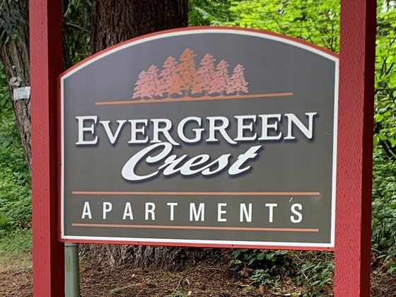 Charming Evergreen Crest Apartments sign surrounded by vibrant flowers and lush greenery, showcasing a welcoming and serene environment.