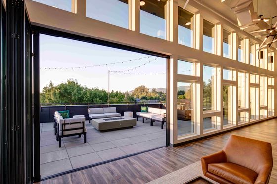 Elegant open living space with a wall of windows leading to a furnished outdoor terrace with scenic views.