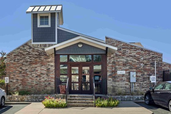 Inviting brick facade of a modern venue with large glass doors and neatly landscaped entrance.