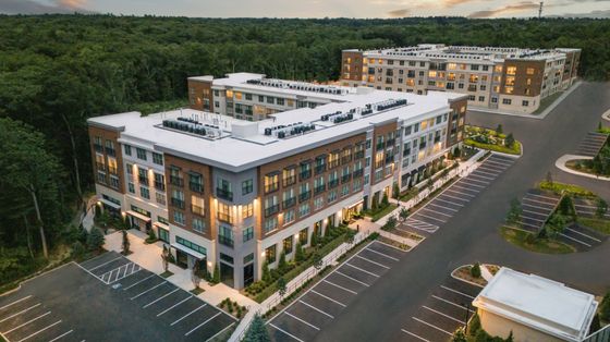 Aerial view of a luxury apartment complex surrounded by lush greenery with ample parking spaces.