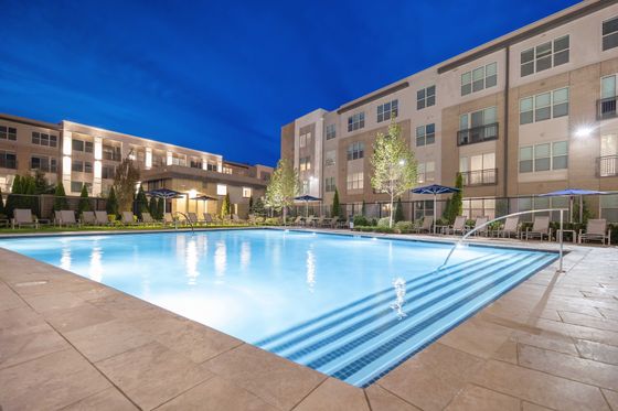Elegant apartment complex with a large illuminated swimming pool at night.