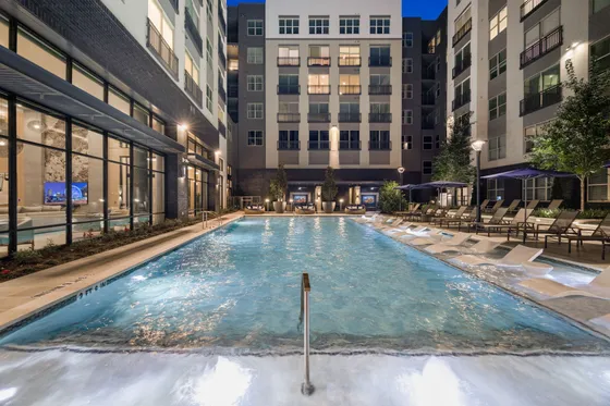Luxurious apartment complex featuring a stunning outdoor swimming pool surrounded by modern architecture and stylish lounge chairs, perfect for relaxation and enjoyment.
